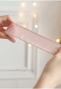 Close-up of pink satin Christmas ribbon with braided silver and white edges