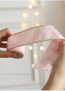 Close-up of pink satin Christmas ribbon with silver woven edges held by hands