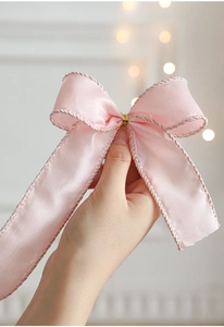 Close-up of pink satin ribbon bow with silver woven edges and gold metallic clasp