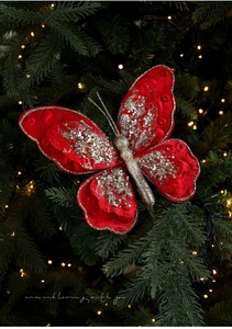 Nahaufnahme eines roten Samt-Schmetterlings mit Goldpailletten am grünen Weihnachtsbaumzweig