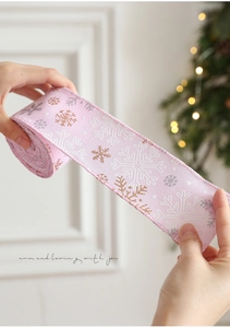 Nastro di Natale rosa con fiocchi di neve glitterati tenuto davanti a un albero decorato