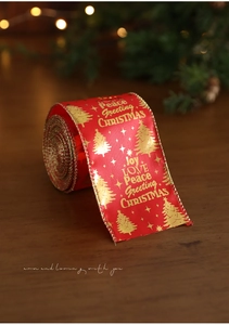 Detail of red Christmas ribbon with gold embossed trees and festive text on wood