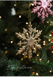 Detailaufnahme einer 11cm glitzernden goldenen Schneeflocke als Christbaumschmuck am Zweig