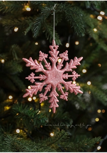 Rosa Glitzer-Schneeflocke hängend an einem Weihnachtsbaumzweig mit warmem Bokeh-Lichteffekt