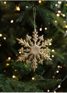 Goldener Glitzer Schneeflocken-Anhänger am Weihnachtsbaum mit warmem Bokeh-Lichteffekt