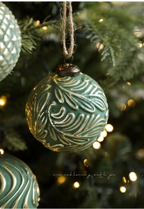 Detailed close-up of dark green Christmas ball with gold leaf veins and jute rope