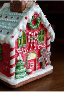 Detail of a glowing Christmas gingerbread house resin ornament with snowy roof and candy canes