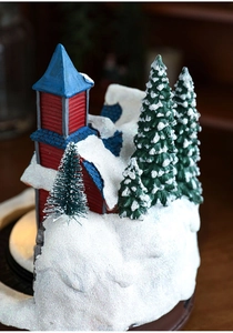 Détail macro de maison de Noël en résine lumineuse avec neige pailletée et sapins nains