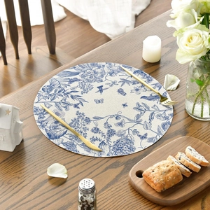 Round linen placemat with blue floral pattern on a dark wood table with candle and cutlery