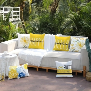 Detail of yellow daisy pillows with HAPPY summer text on a sunny outdoor sofa