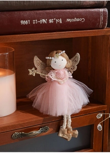 Detail of plush angel doll with pink mesh skirt and golden wings on a wooden shelf