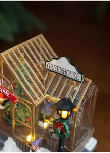 Detailed close-up of a glowing Christmas greenhouse model with mini tree and LED lights