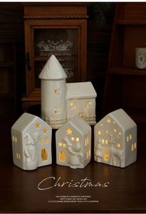 Close-up of four white ceramic Christmas houses with star cutouts and warm glowing LED light