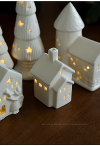 Macro shot of white ceramic Christmas house with warm LED light through star-shaped cutouts