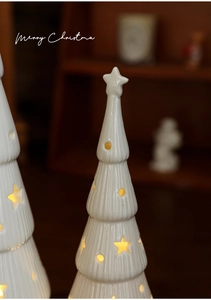 Close-up of white ceramic Christmas tree lanterns with warm glowing star cutouts