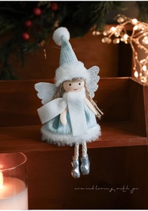 Detail of plush Christmas angel doll with blue hat and silver sequin wings on wooden shelf
