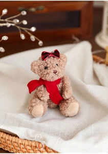 Close-up of curly brown teddy bear plush with a red sequin bow and scarf in a basket