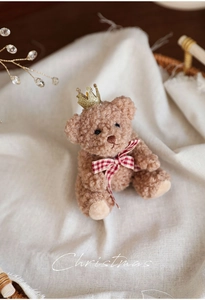 Detail of a brown curly teddy bear with golden crown and red plaid bow for Christmas