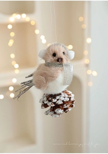 Macro shot of plush bird ornament on a snowy pine cone with wood and warm bokeh light