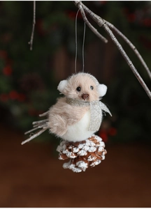 Close-up of plush bird ornament with silver scarf on snowy pine cone base