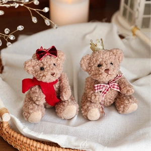 Cute brown teddy bear plush pendants with red bow and gold crown in a cozy gift basket