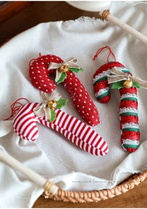 Detail of three fabric candy cane ornaments with bows and bells in a rustic basket
