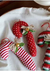 Detailed view of red fabric candy cane ornaments with linen bows and gold bells for Christmas