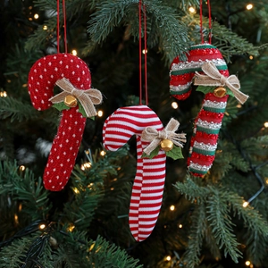 Three-piece fabric Christmas candy cane ornaments with bows and bells on a lit tree