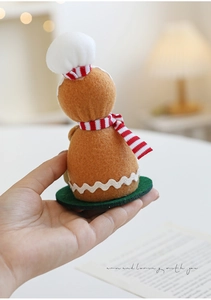 Handmade gingerbread man wool felt doll detail with chef hat and scarf on a green base