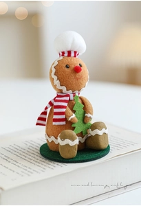 Detail of plush gingerbread man with chef hat holding a felt Christmas tree on a green base