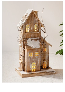 Détail d'une maison de Noël en bois illuminée avec neige artificielle et branches de pin