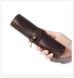 Detail of vintage brown crazy horse leather pen roll with a metal key charm and orange stitching