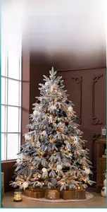 Nahaufnahme weißer verschneiter Weihnachtsbaum mit Karoschleifen, Kugeln und warmen LED-Lichtern