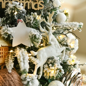 White reindeer and star hanging ornaments with wooden Christmas sign on snowy pine branches