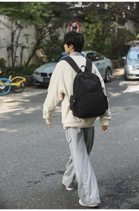 Outdoor-Straßenszene mit einem schwarzen Nylon-Rucksack mit breiten Gurten und Reißverschluss