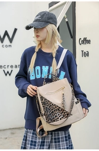 Close-up of leopard print backpack with tassel charms and metallic zippers on beige base