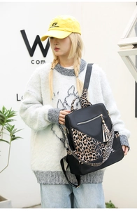 Detail of black nylon backpack featuring leopard print trim and matching tassel on model