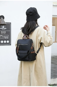Outdoor view of a black nylon backpack with brown leather trim and tassel on a model