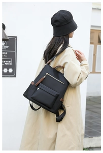 Outdoor side view of a large black nylon backpack with brown leather tassels and gold accents