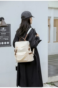 Outdoor shot of cream nylon backpack with brown leather handles on person wearing black coat