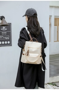 Detail view of stylish cream-white nylon backpack with brown leather handle and fringe zip