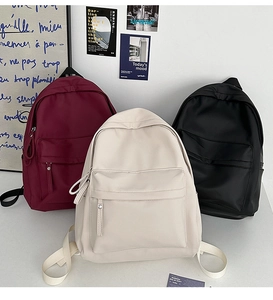 Close-up of durable nylon backpacks in wine red, cream white, and black with front pockets