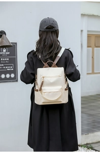 Rear view of a stylish off-white backpack with brown leather accents on a model