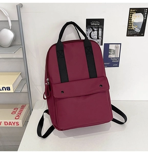 Detail of burgundy waterproof backpack showing front pocket with snaps on white desk