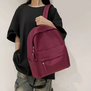 Detailed view of the burgundy nylon backpack with zipper pocket and side compartments