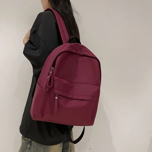 Detail view of the burgundy nylon backpack with a spacious front pocket for daily travel