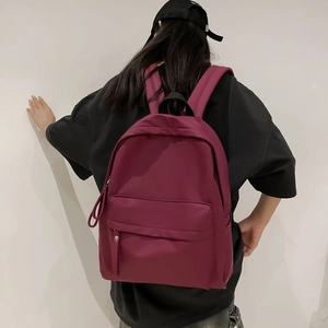 Rear view of a burgundy waterproof nylon backpack worn by a model on a white background