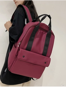 Detail shot of a burgundy nylon laptop backpack featuring dual snap buckles and wide handles