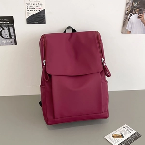 Detail of burgundy backpack with top flap and side pockets on a minimalist desk