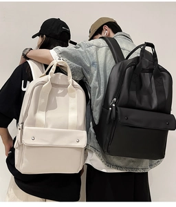 Detail view of black and beige minimalist waterproof backpacks with front pocket and top handle